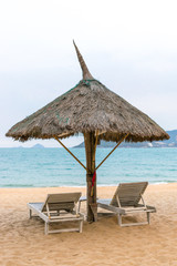 Big parasol of straw with two loungers on sandy beach for relax