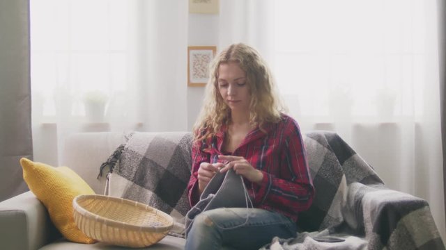 Zoom in of woman sitting on sofa, knitting in home and looking in camera