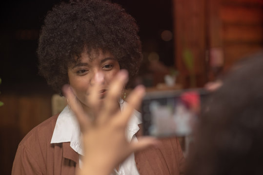 Woman with afro being photographed on cellphone
