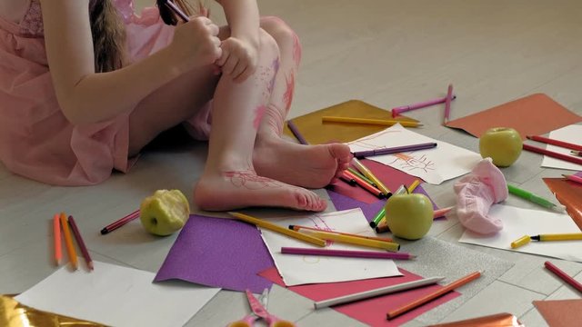 little girl draws on her feet with felt-tip pens, children's creativity, development