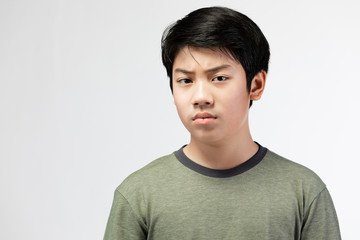 Portrait Young Asian boy over gray background, be upset; have a bad temper emotional portrait of teen boy wearing t-shirt. Thoughtful teenager, isolated on white background. 