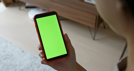 Woman hold mobile phone with green screen at home