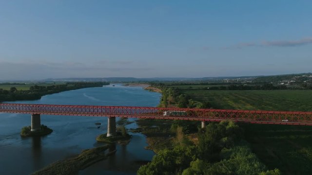 Traveling over a red metal bridge, sunset time, in Goleg&atilde;, Santar&eacute;m, Portugal. Green landscape and river views. Soft and bright light. Chamusca