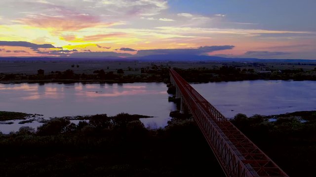 Traveling over a red metal bridge, sunset time, in Goleg&atilde;, Santar&eacute;m, Portugal. Green landscape and river views. Soft and bright light. Chamusca