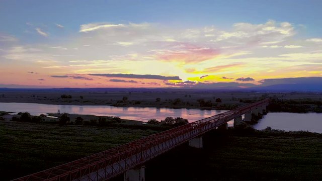 Traveling over a red metal bridge, sunset time, in Goleg&atilde;, Santar&eacute;m, Portugal. Green landscape and river views. Soft and bright light. Chamusca