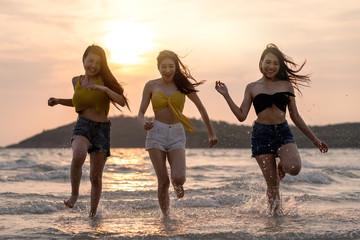 Group of Three asian beautiful attractive young woman playing and running on the beach at the sea. Group of happy friends runs to the sea with tropical beach at sunny evening. Beach holidays concept