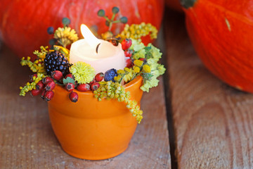 Orange candle holder decorated with autumn flowers and other plants