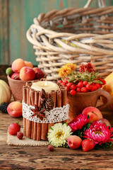 Candle decorated with cinnamon sticks among autumn fruits and flowers.
