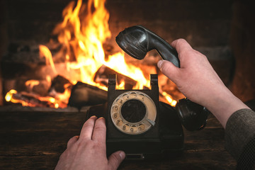 Man is holding in hands a black old phone on a burning fire in fireplace background. Hotline concept.