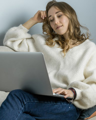 Girl sitting on sofa with laptope, hold big white mag cacao with marshmallow and listen music. Home...