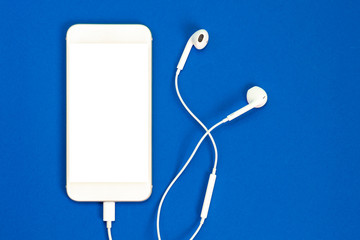 Fototapeta na wymiar White smartphone on the blue background with headphones. View from above.