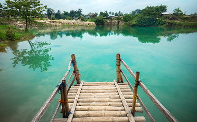 Naklejka premium Wooden Pier on Green Blue Lagoon, Tropical Paradise. Traditional Bamboo Pier or Jetty on Lakeside. Concept of New Beginning of Exploration, Discovery or Exit Your Comfort Zone