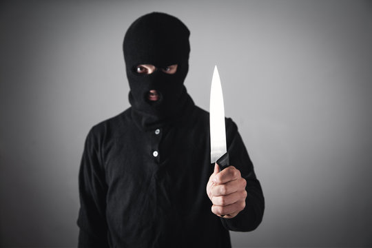 Killer in black mask threatening with knife. Crime and robbery concept