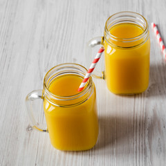 Fresh orange juice in glass jars over white wooden surface, low angle view. Closeup.