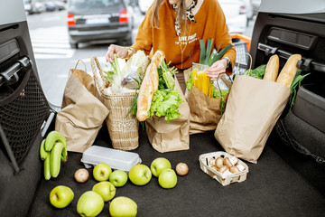 Woman packing shopping bags with fresh food into the car trunk, view from the vehicle interior