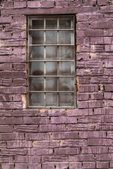 Brick wall of the building of darkly red color with a window on the middle. Glass not transparent from dirt and dust. At a window a thick strong lattice