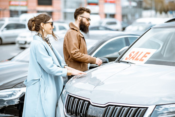 Young stylish couple choosing luxury car to buy on the open ground of the dealership