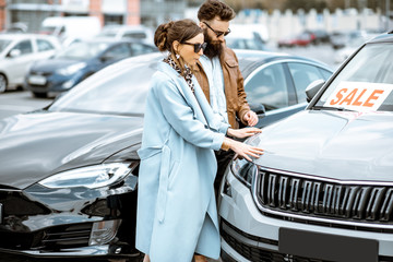 Young stylish couple choosing luxury car to buy on the open ground of the dealership