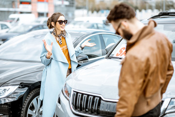 Young stylish couple choosing luxury car to buy on the open ground of the dealership