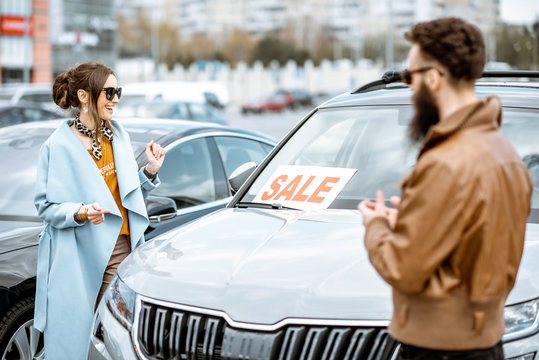 Young stylish couple choosing luxury car to buy on the open ground of the dealership