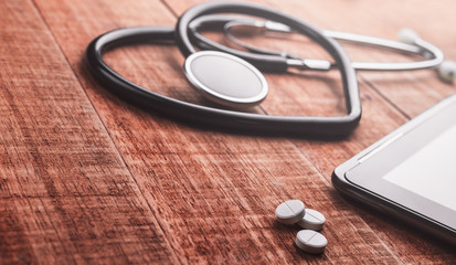 Stethoscope heart shaped and pills on wooden background.Heart concept, cardiology