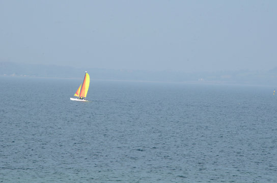 A boat with colorful sails on the ocan in slight mist.