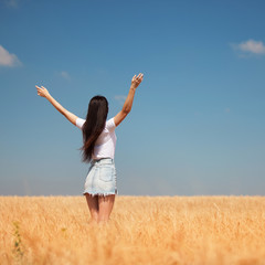 Happy woman enjoying the life in the field Nature beauty, blue sky and field with golden wheat. Outdoor lifestyle. Freedom concept. Woman jump in summer field