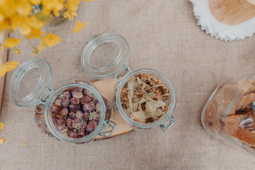 Red clover and linden flowers in glass jars on the table, jars with cookies and near. Top view, horizontal orientation. 