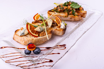 Appetizer bruschetta with cheese, honey, walnut and dry orange slices on white background. Close-up.