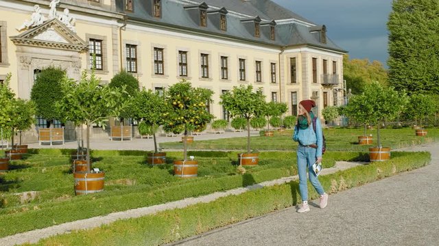 Hannover, Germany. A grove of citrus mandarins and oranges planted near a beautiful medieval palace. Young female caucasian tourist with a map in her hands walks and enjoys the sunset sun. Slow Motion