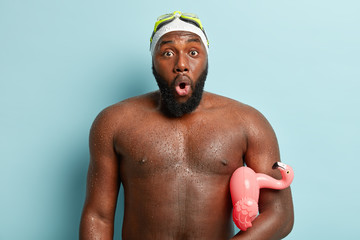 Photo of astonished black man with wet skin, shocked to see many people at beach, swims in sea with...