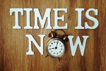 Time Is Now alphabet letter with alarm clock on wooden background