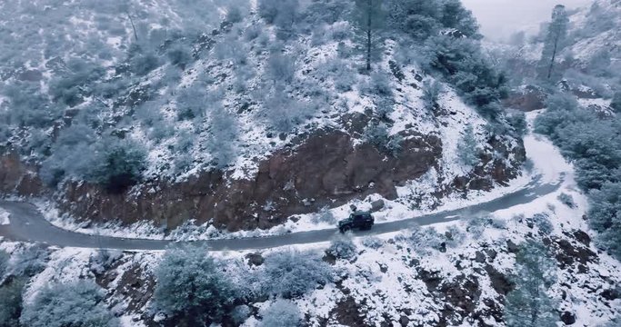 Jeep driving off-road on a cliffside in a snow storm. Making fresh tracks around a mountain side and carefully moving forward. Shot from above in 4k.mov