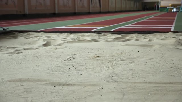 Girl athlete performing long jump into sandbox