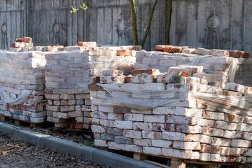 Old bricks stacked on a wooden frame partially covered with polyethylene.