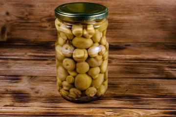 Glass jar with canned mushrooms on wooden table