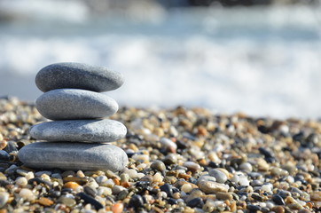 Zen pyramid of spa stones on the blurred sea background. Sand on a beach. Sea shores. Water waves texture. Place for text. concept of balance and spirituality