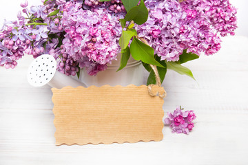 Lilac flowers and empyt card on white wooden background, copy space