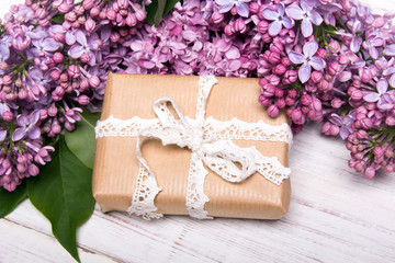 Lilac flowers, gift box on white wooden background