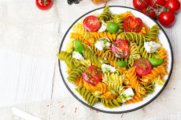 Italian food - Salad with colorful pasta, cherry tomatoes, feta cheese and fresh basil on white...