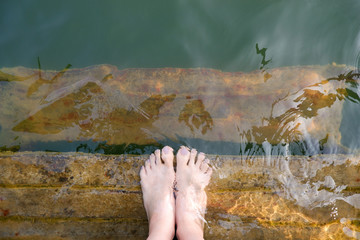 Feet and Purple Pedicure of Woman in Green Water, Top view. Beautiful Asian Young Female Body Legs and Barefoot on a Wooden Bridge Background. Cropped Image of People Foot Under Aqua Water on Summer.