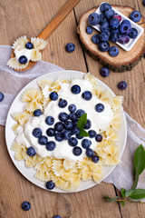 Tasty pasta with fresh organic blueberries and vanilla cream. Sweet dinner on retro wooden table.