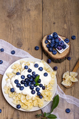 Tasty pasta with fresh organic blueberries and vanilla cream. Sweet dinner on retro wooden table.