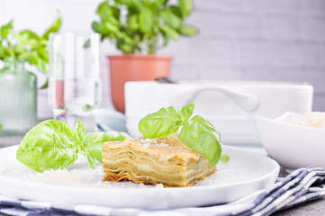 Traditional Italian cuisine for lunch. Lasagna with pesto and basil in a porcillo plate. White...
