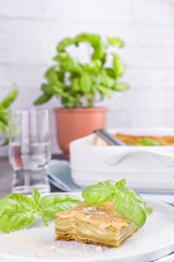 Traditional Italian cuisine for lunch. Lasagna with pesto and basil. White dishes on the table.Copy space