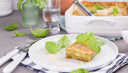 Traditional Italian cuisine for lunch. Lasagna with pesto and basil in a porcillo plate. White dishes on the table. Banner