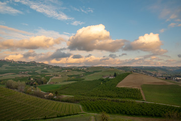 Panoramic view of the vineyard hills of the Langhe region in Piedmont, become Unesco World Heritage Site since 2014, with a cloudy blue sky in springtime, Italy 