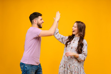 Photo of young couple man and woman giving high five isolated over yellow background