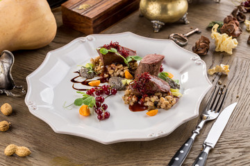 Deer chops with pearl barley and cranberry sauce on wooden table