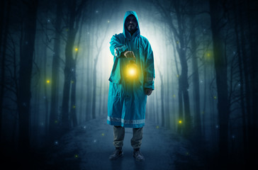 Fototapeta na wymiar Man in raincoat coming from dark forest with glowing lantern in his hand concept 